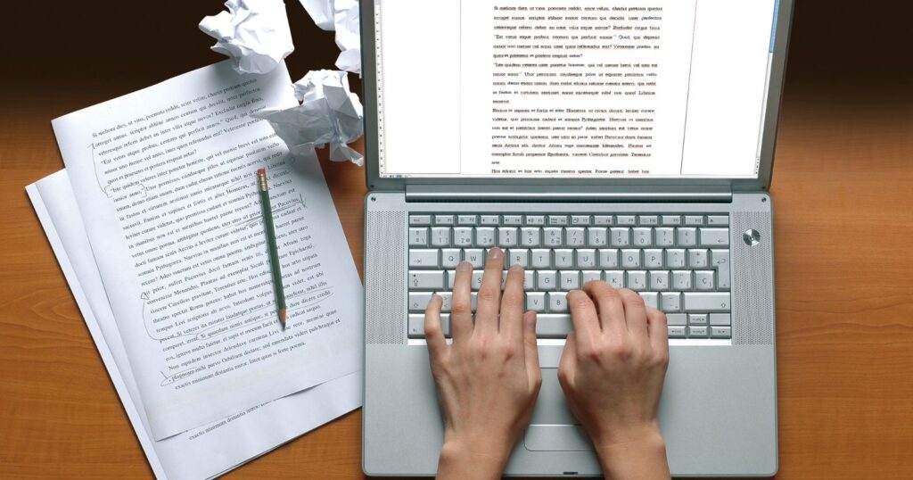 A contemporary writer typing on a laptop with papers and a pencil, engrossed in their work.