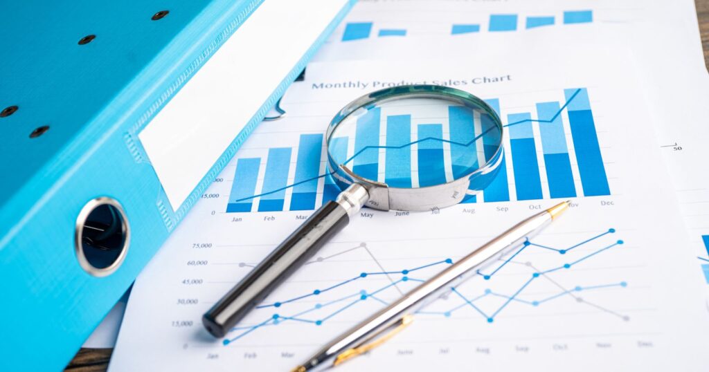 Business documents and financial charts with magnifying glass on wooden table. Advanced Data Analysis.