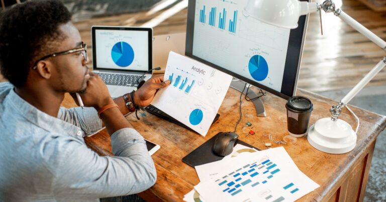 A person utilizing Google Analytics on a laptop and monitor while seated at a desk.