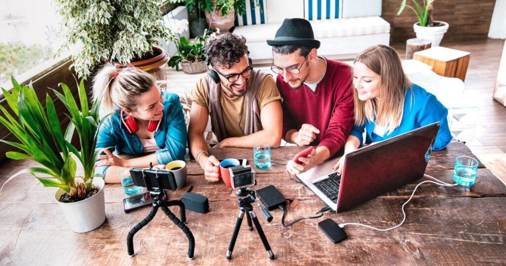 Four individuals gathered around a table, engrossed in a laptop and camera, discussing social media content.