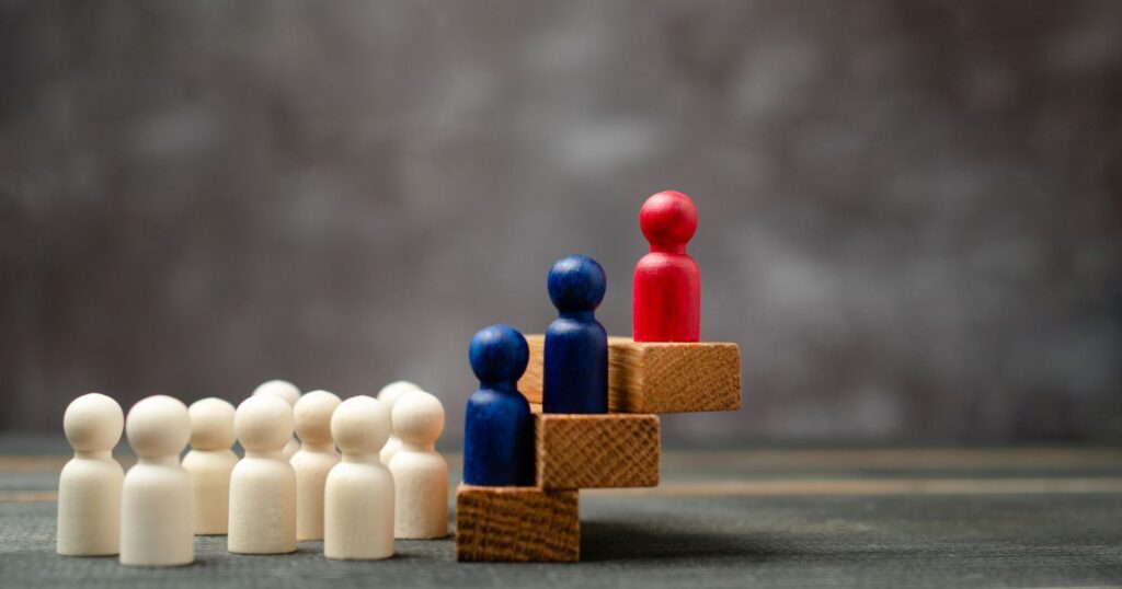 A group of wooden people standing on a block, symbolizing unity and teamwork. "Leveraging Platforms for Maximum Impact."