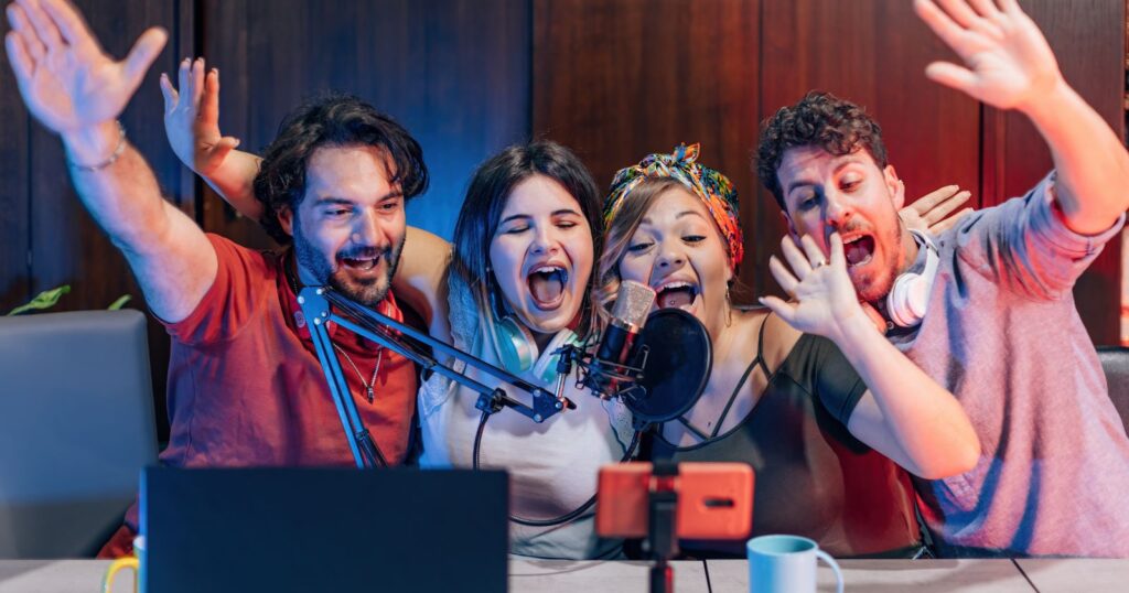 four individuals enthusiastically raise their hands while recording.