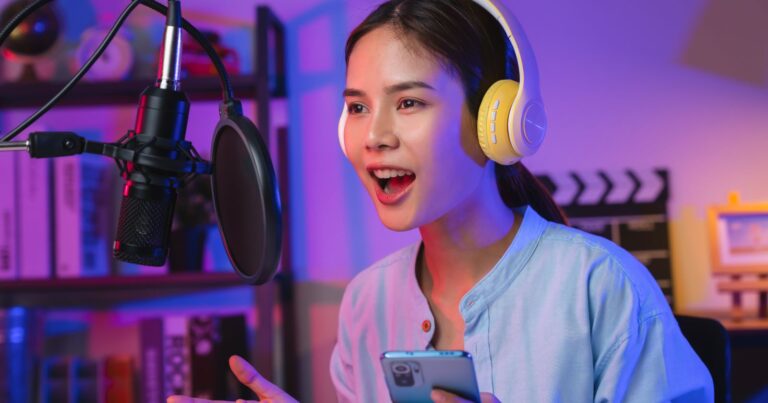 A woman wearing headphones and holding a cell phone stands in front of a microphone, representing content crafting in today's digital world.