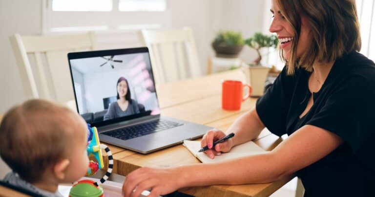 A woman and baby sit at a table with a laptop, symbolizing work-life balance for an entrepreneur.