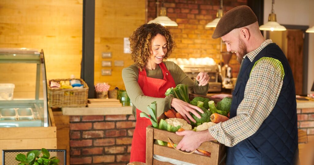 A man and woman stand in front of a box of vegetables. Text: "Choose Local and Seasonal Produce"