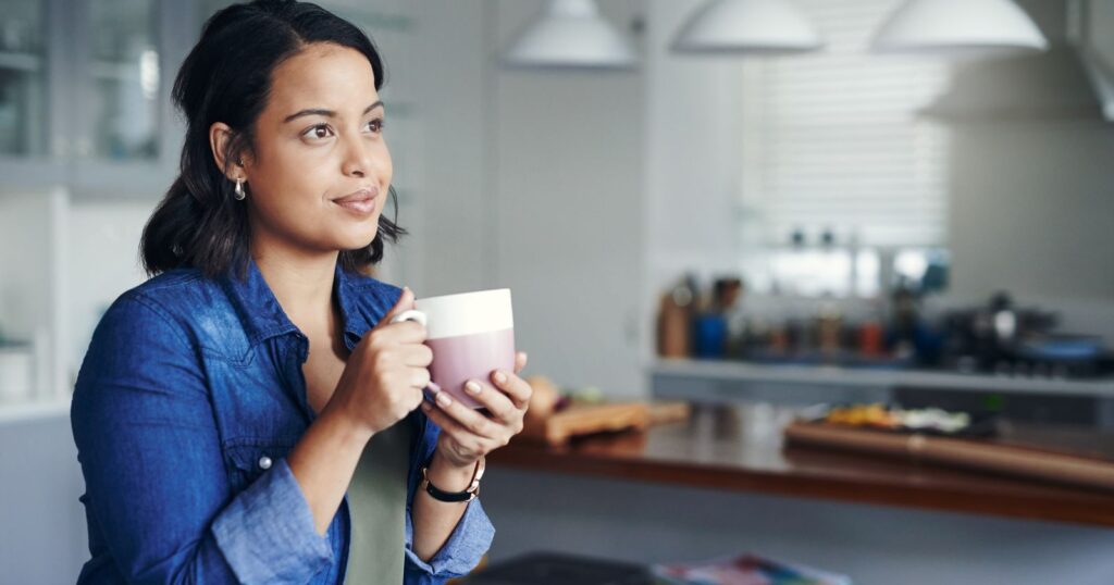 A woman in her kitchen, holding a cup of coffee, embodies the spirit of reflection, adaptation, and growth.