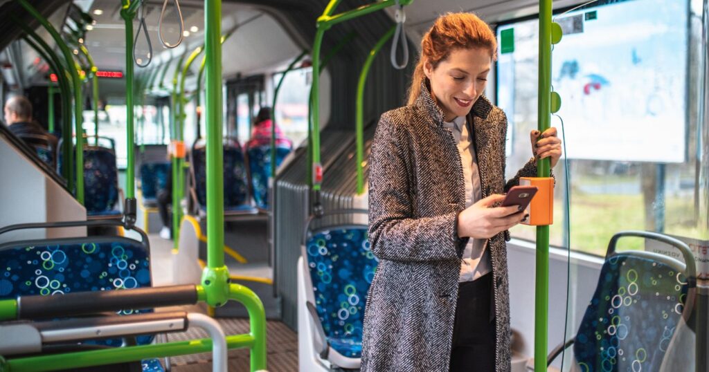 A woman on a bus, engrossed in her phone, exemplifying sustainable transportation.