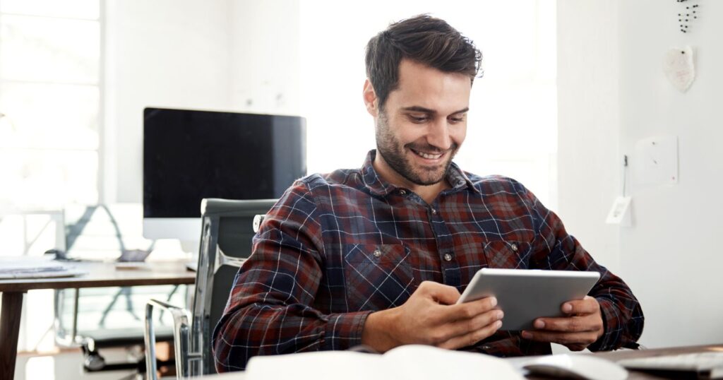 A man sitting at a desk, focused on a tablet, embodying the motto "Work Smarter, Not Harder."